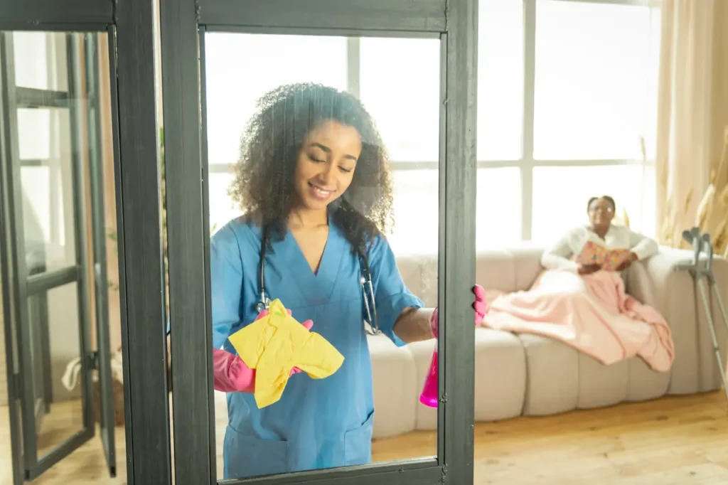 Female support worker cleaning a window inside the home
