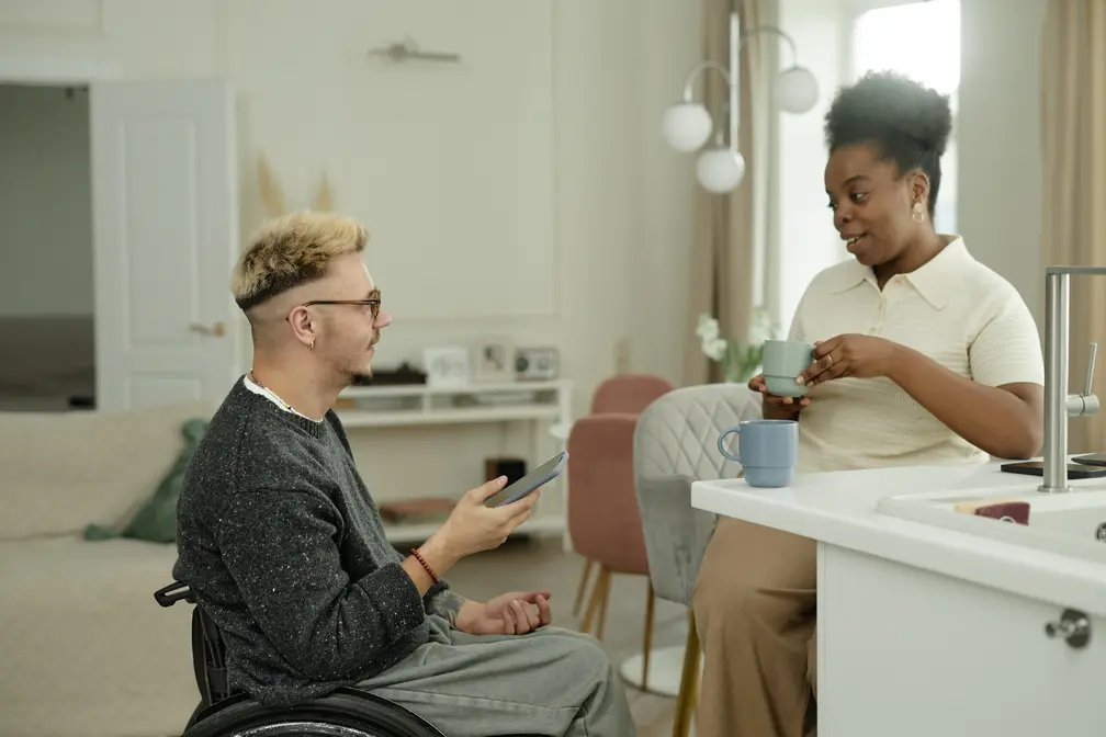 Disabled man talking with female support worker in kitchen